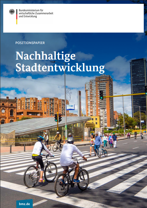 Das Titelblatt des Positionspapiers des BMZ zu nachhaltiger Stadtentwicklung zeigt mehrere Radfahrer auf einer breiten Straße in einer Großstadt, umgeben von mehrstöckigen Gebäuden aus roten Backsteinen und blauem Himmel mit Wolken.